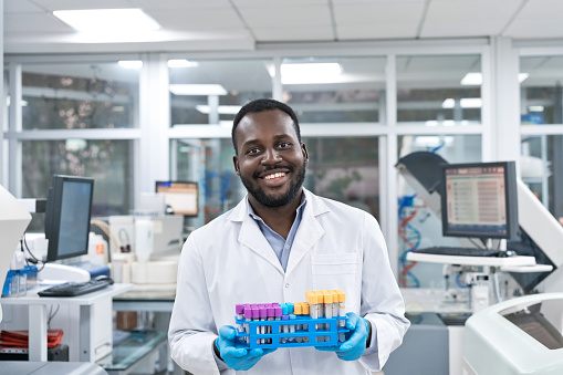 Portrait of smiling young male scientist holding sample test tube rack at laboratory