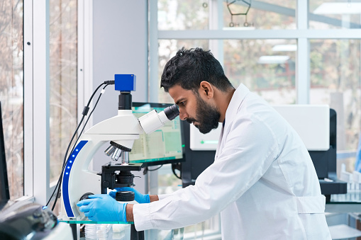 Side view of young male scientist looking through microscope at laboratory