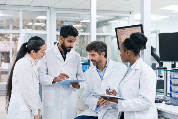 istock Team of biochemists discussing over while writing on clipboards at laboratory 1746647477