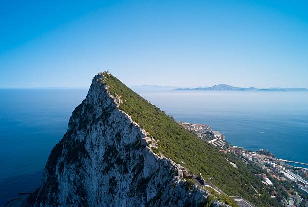View of Gibraltar Rock surrounded by the ocean "Gibraltar Rock, overlooking the Mediterranean Sea, with the African coast and Atlas Mountains visible in the background behind a veil of mist." gibraltar photos stock pictures, royalty-free photos & images