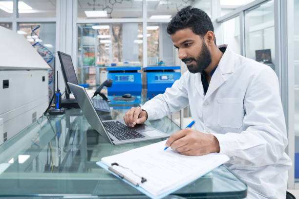 istock Young male biochemist using laptop while writing on clipboard at laboratory 1746650566
