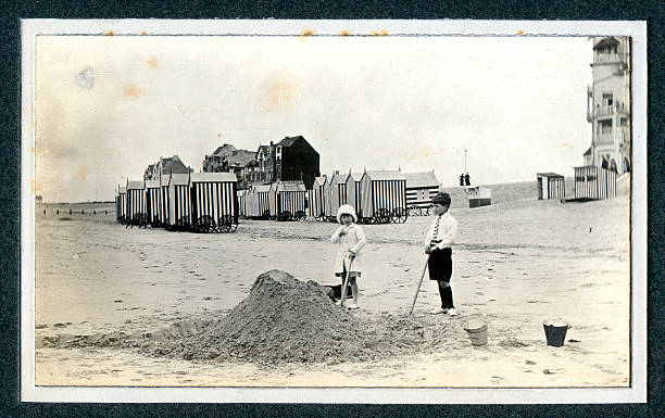 Edwardian children playing at the seaside - Vintage Photograph Vintage photograph of two Edwardian children playing in the sand at the seaside. Knokke, Belgium. beach hut photos stock pictures, royalty-free photos & images
