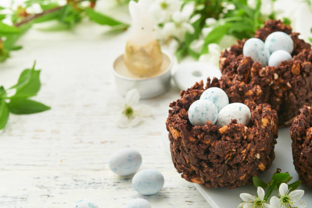 istock Easter brunch or breakfast. Easter chocolate nest cake with chocolate candy eggs, traditional hot cross buns and deviled eggs with bouquets of blooming apple trees. Spring Easter holiday food concept. 1746657013