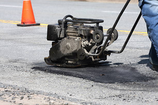 Pot Hole Repair, Series A construction worker operates a compactor to compress freshly poured asphalt in a pothole on a road repair project. sinkhole stock pictures, royalty-free photos & images