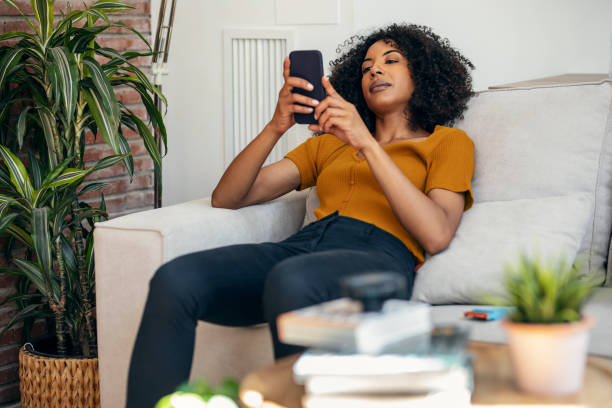 istock Smiling woman using her mobile phone while sitting on sofa at home. 1746660043