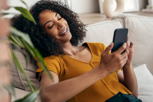 istock Smiling woman using her mobile phone while sitting on sofa at home. 1746660046