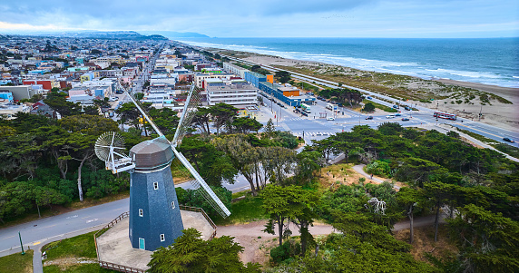 Image of Aerial blue murphy windmill with white blades overlooking city of hoses and ocean with beach