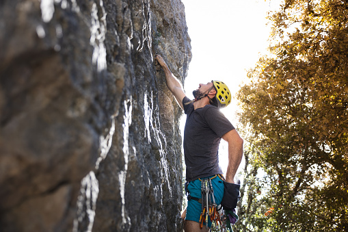 Athletic man climbs an overhanging rock with rope and carabiners, lead climbing.  Rock climber concept.