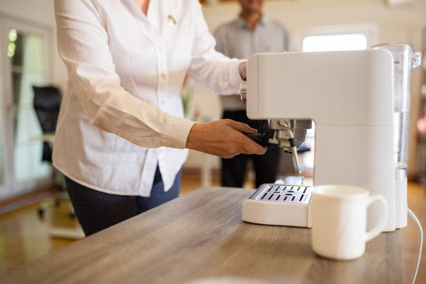 Mature woman preparing coffee on coffee maker in modern office.