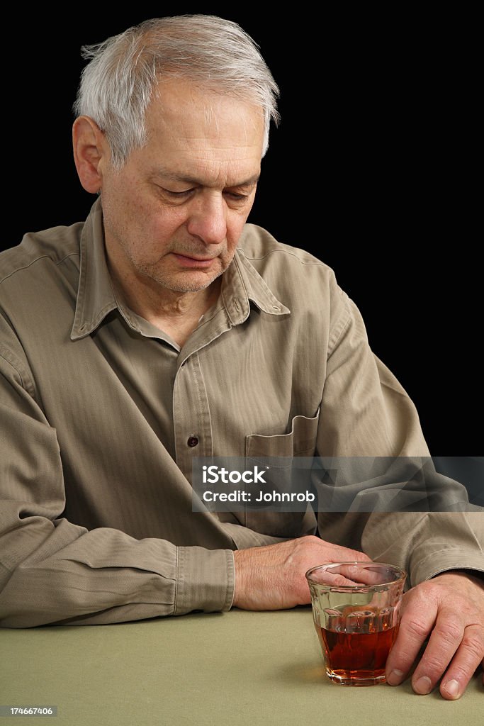 Senior man sitting at table in depressed state with cocktail Senior man sitting at table in depressed state with cocktail looking down in contemplation at drink with sad eyes. Black background. 60-64 Years Stock Photo