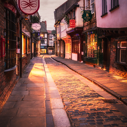 Multiple shops and restaurants at dawn on The Shambles in York's ancient city centre, a famous medieval cobbled street.