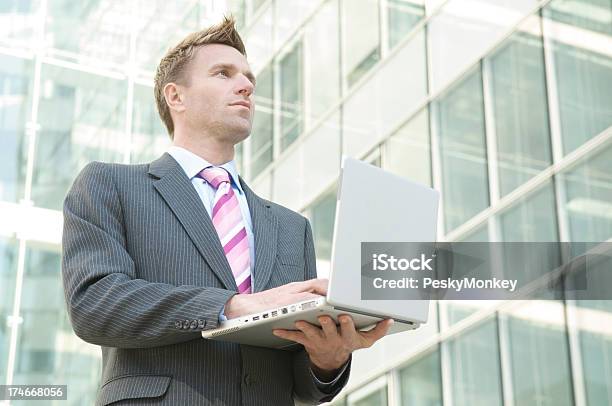 Businessman Stands In Corporate Courtyard Using Laptop Computer Stock Photo - Download Image Now