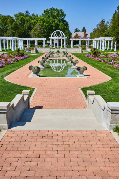 istock Brick pathway leading down to pools with stone flowerpots and flowers with white trellises 1746683374