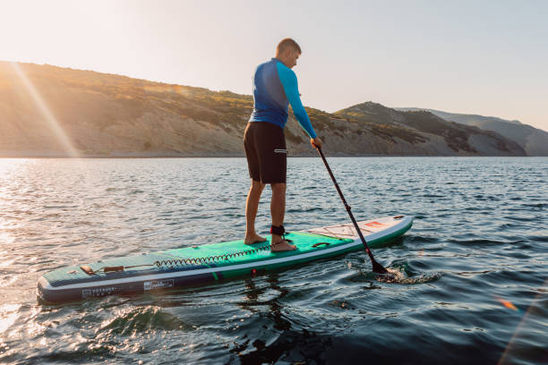 athletischer mann auf stand-up-paddle-board am meer. training auf dem sup-board in ruhiger see. - editorial women paddleboard surfboard stock-fotos und bilder