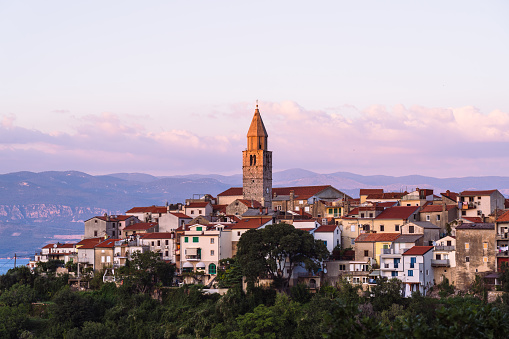 small old croatian village with church clocktower on hill overlooking the adriatic sea on sunny evening with some clouds over mainland in background
