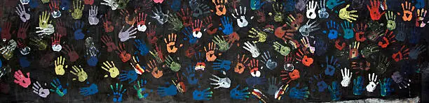 "colorful children's handprints on a textured black wall - fragment of a busstop wall in Bali, Indonesia"