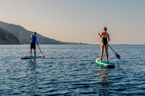 August 06, 2023. Budva, Montenegro. Couple rowing on stand up paddle board. Summer vacation on Red paddle SUP board in quiet sea.