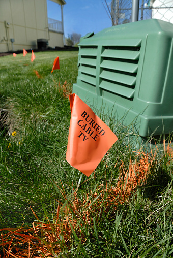 Orange flags mark the path of buried TV cable next to a junction box between houses in a subdivision.