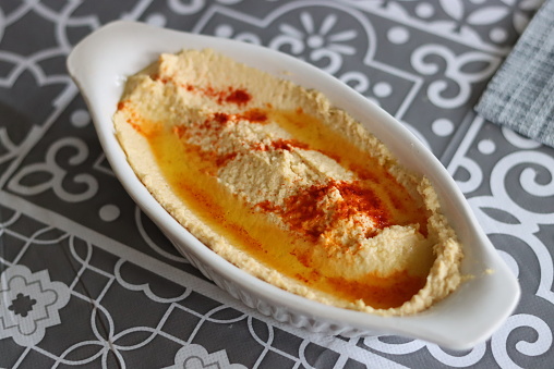 Homemade hummous with olive oil and paprika decoration in a small white dish on a table