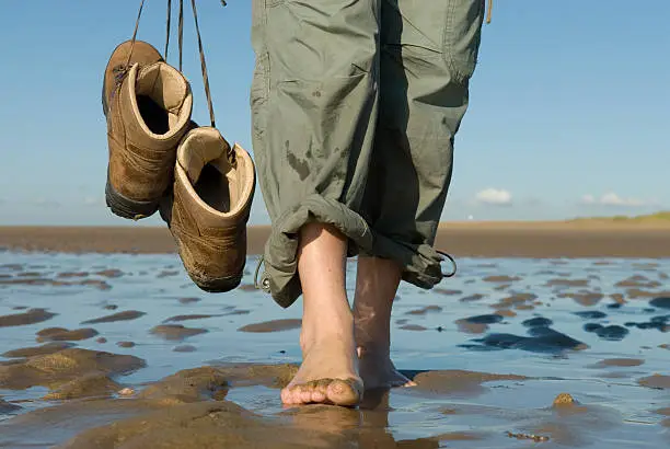 "Walking with bare foot on the beach. Relaxing walk with the toes in the sand, to feel the nice cool water. The person is holding hiking shoes along side so they will dry inside after a long day of hiking.More images of the dutch coast:"