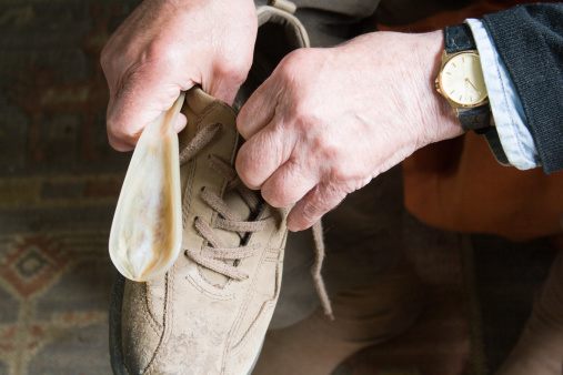 The hands of a senior man sruggling with his lace-up shoes. Difficulties of old age.