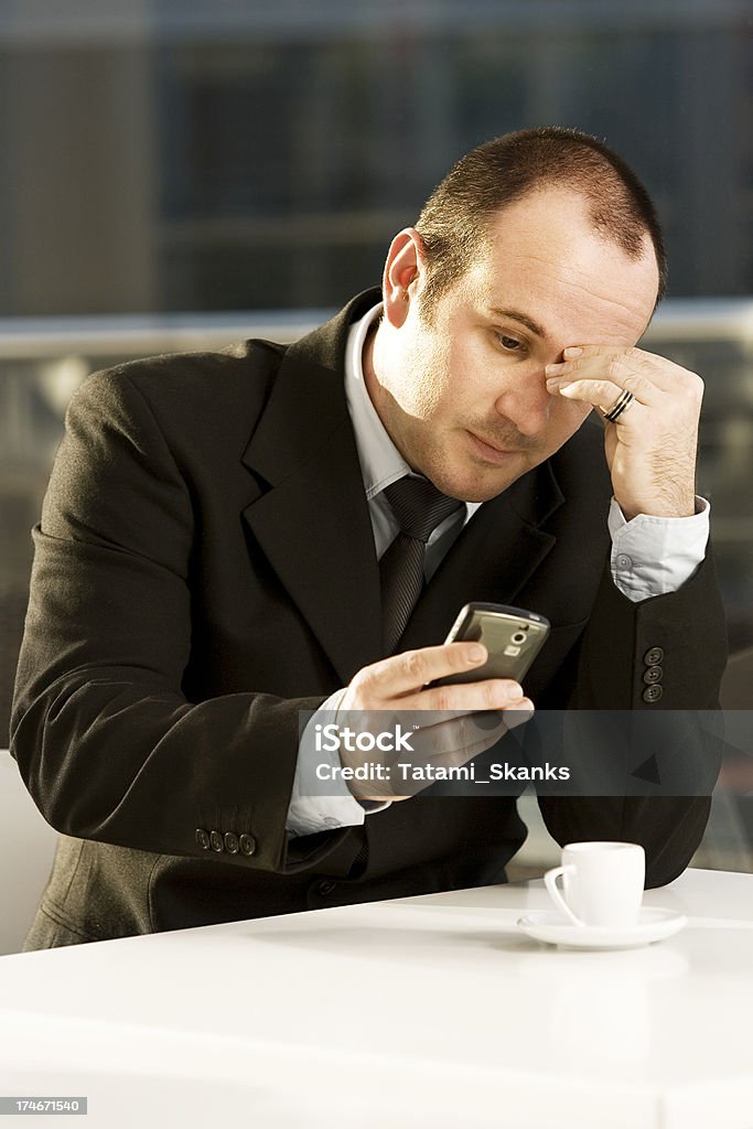 Businessman reads mail "A distressed businessman in coffee shop reads an email on his cell phone while drinking espresso. Black suit, white shirt and tie." Black Color Stock Photo