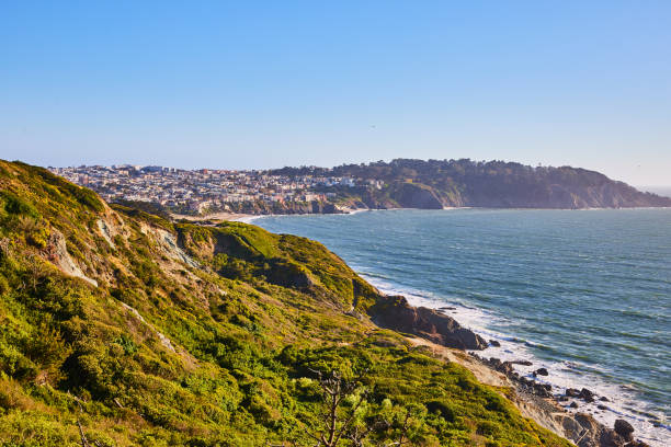 istock Green hilly coastline mountain with distant city and waves rolling into shore in ocean bay 1746716577