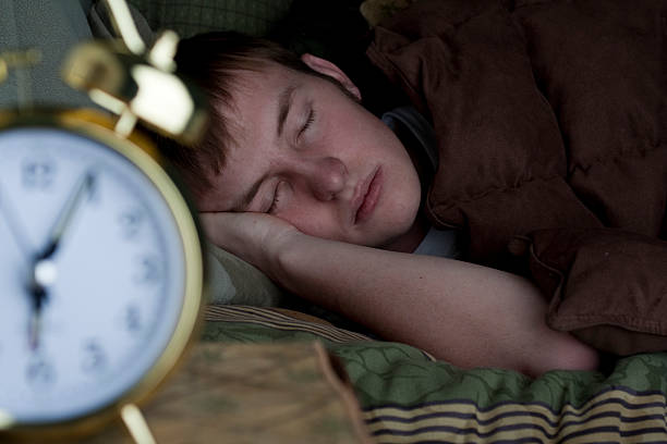 Teenager girl sleeping in a white bed. Alarm clock in the foreground on pile of books
