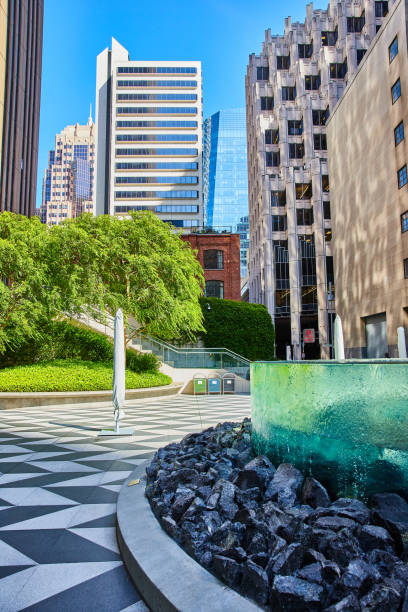 istock Park with unique glass wall with water running down sides toward rocks and checkered sidewalk 1746731037