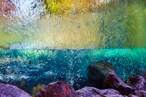 Image of Reflective colorful surface of glass with water falling down sides to purple and black rocks