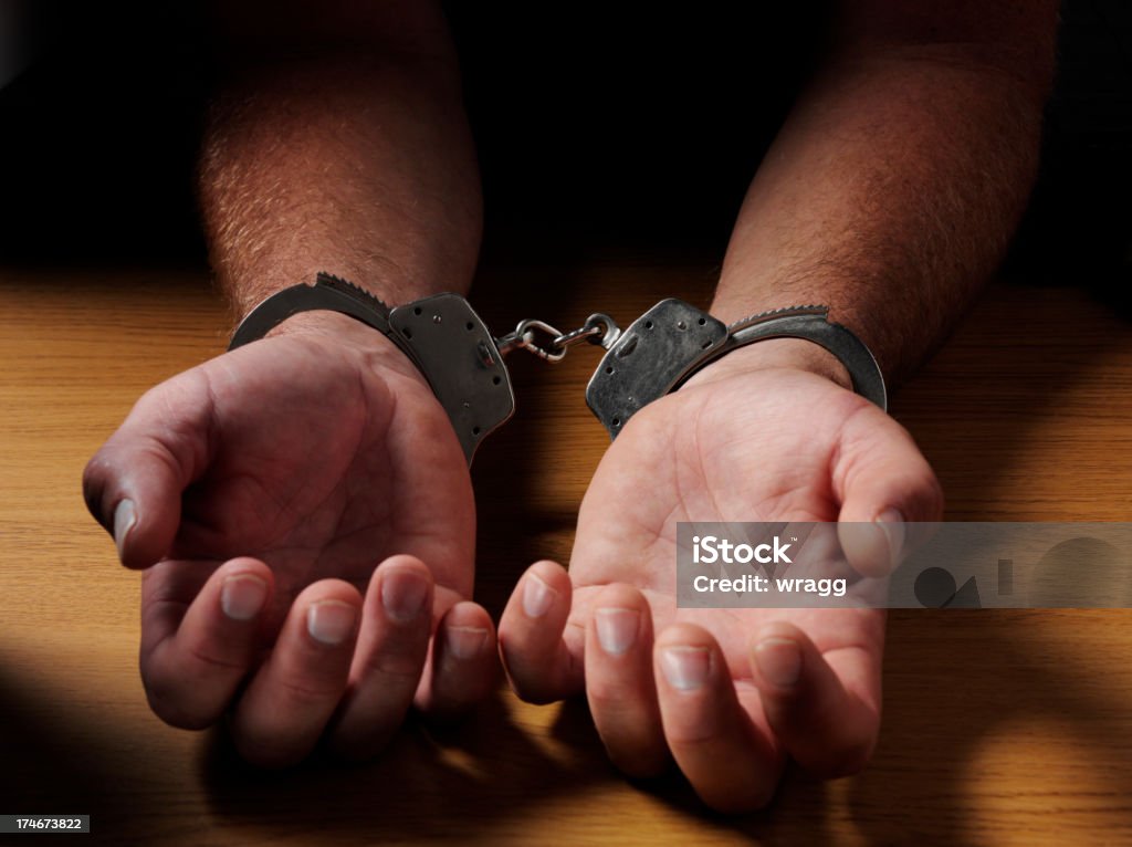 Hands in Handcuffs Hands in handcuffs on a wooden desk. Alloy Stock Photo