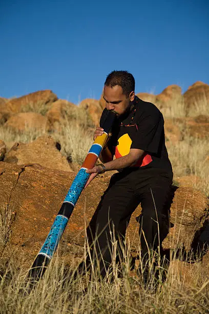 An Aboriginal man playing a colouful didgeridoo in the outback of Australia.