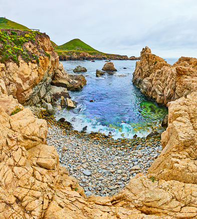 Image of Rocky coastal cove panorama with blue water and green patch under waves