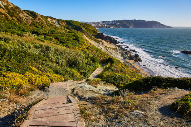 istock Stairs with no railing going down green hill toward rocky shore with small beach and waves 1746754112
