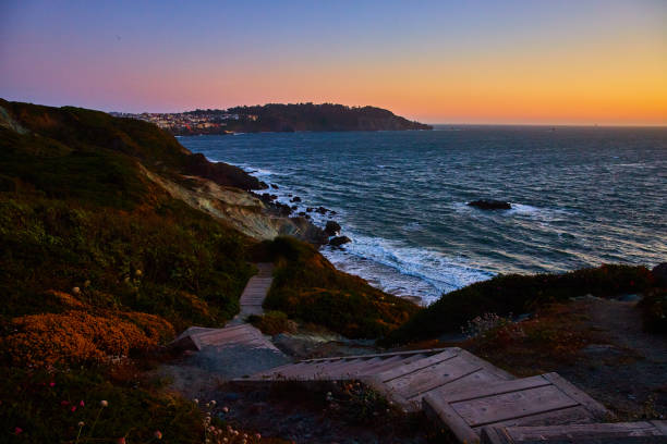 istock Steps going down hill toward blue ocean with sunset sky and distant city above cliff 1746754670