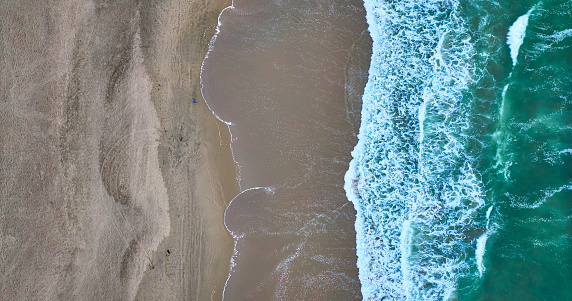Image of Straight down aerial green ocean waves on right with wet sandy beach on left