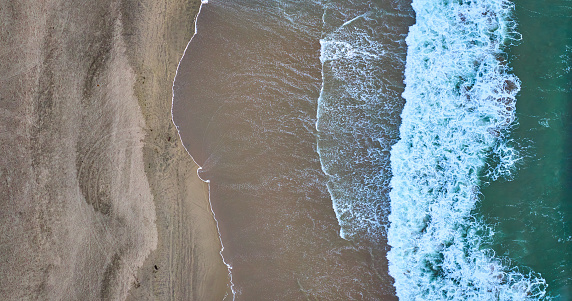 Image of Straight down aerial of green ocean waves on right with wet sandy beach on left
