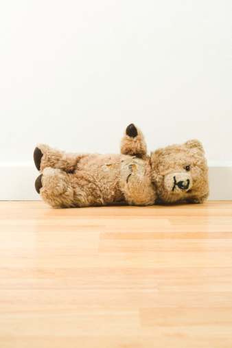 Teddy bear lying on a hardwood floor.