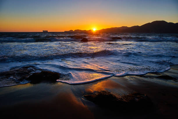 istock Sunset over mountains with blue waves crashing into sandy beach 1746760941