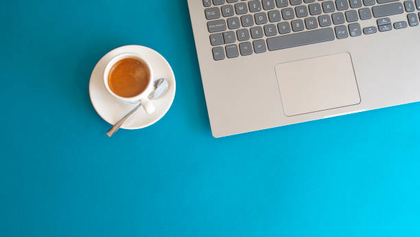 istock White cup with coffee and shiny metal spoon next to laptop on blue background 1746761477