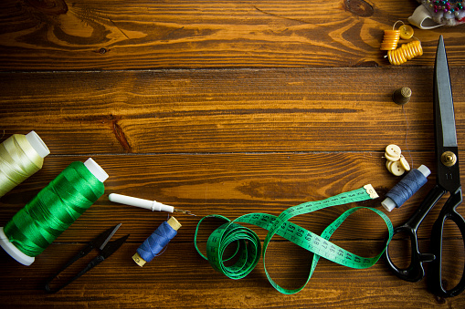a set of tools and threads for sewing clothes, on a wooden background.
