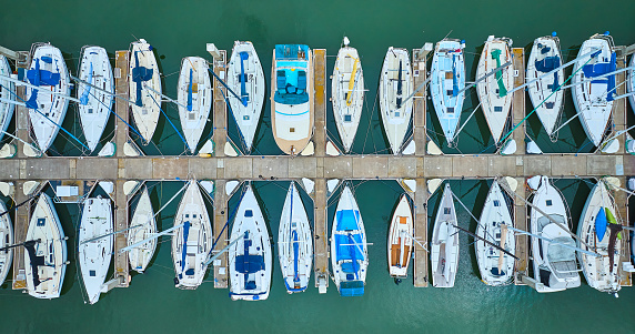 Image of Variety of boats and yachts docked at pier in aerial straight down shot of teal ocean water