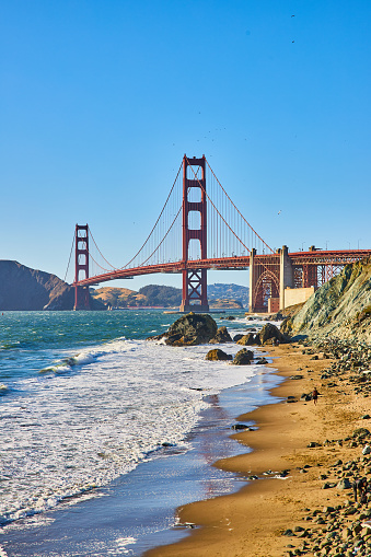 Image of View of Golden Gate Bridge from sandy beach with waves crashing against rocks