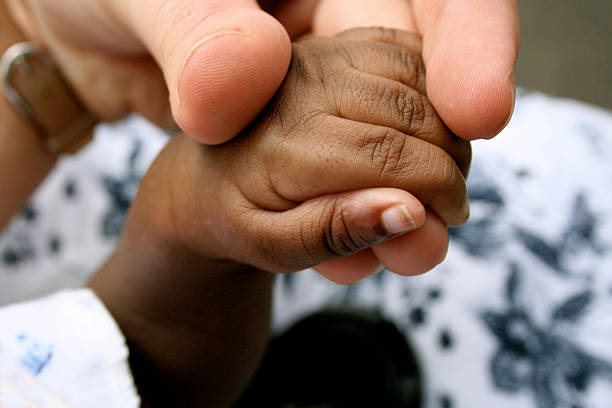 African Baby Hand "The hand of a baby orphan from Liberia, West Africa, being held in the fingers of a volunteer." premature stock pictures, royalty-free photos & images