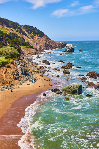 Image of Wet sandy beach with foamy waves and rocky coastline on gorgeous summer day