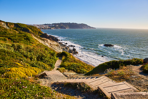 Image of Wooden stairs going down green hill toward rocky shore with small beach and waves