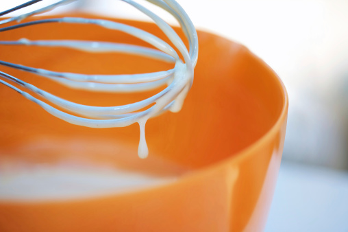 Whisk with dripping batter in orange mixing bowl