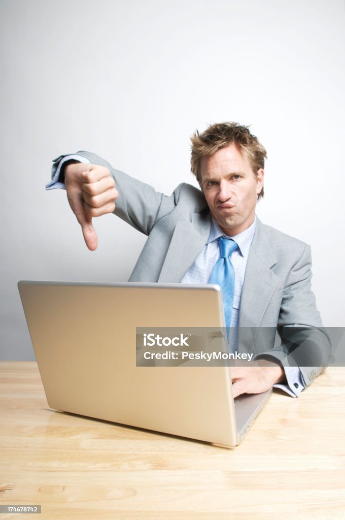 Office Worker Gives a Thumb Down Office worker sitting in front of his laptop gives the camera one thumb down Business Stock Photo