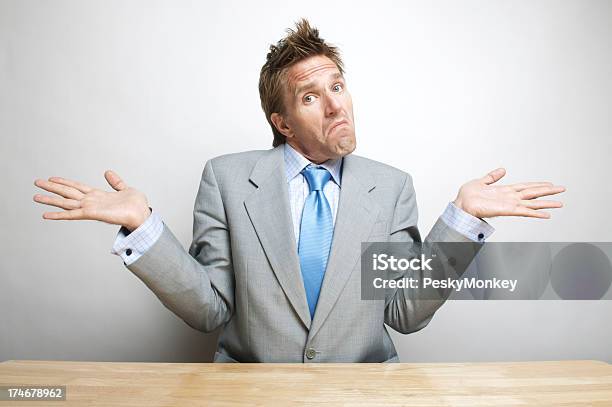Doubtful Confused Office Worker Businessman Shrugs Shoulders At His Desk Stock Photo - Download Image Now