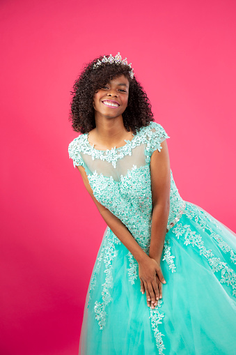 Hispanic girl celebrating her sweet 16 in a pick background wearing a blue dress looking as a princess with a tiara